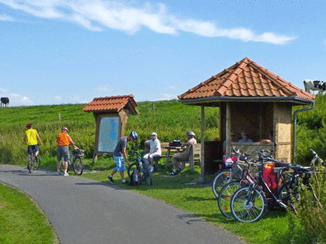 Eine Gruppe Fahrradfahrer pausiert in einer Holzhütte am Deich