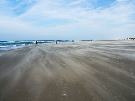 Starke Wellen und Wind, der mit Sand über den Strand fegt